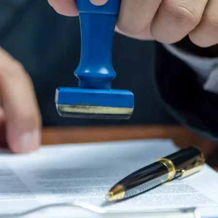 Mano aplicando un sello azul sobre un documento oficial junto a un bolígrafo, símbolo de certificación ISO 50001